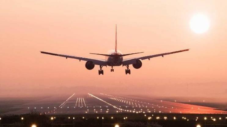 Комерцијални авион на најдужој авионској линији прилази писти у залазак сунца, са ужареним светлима писте и сунцем ниско на небу, стварајући топлу и спокојну атмосферу.